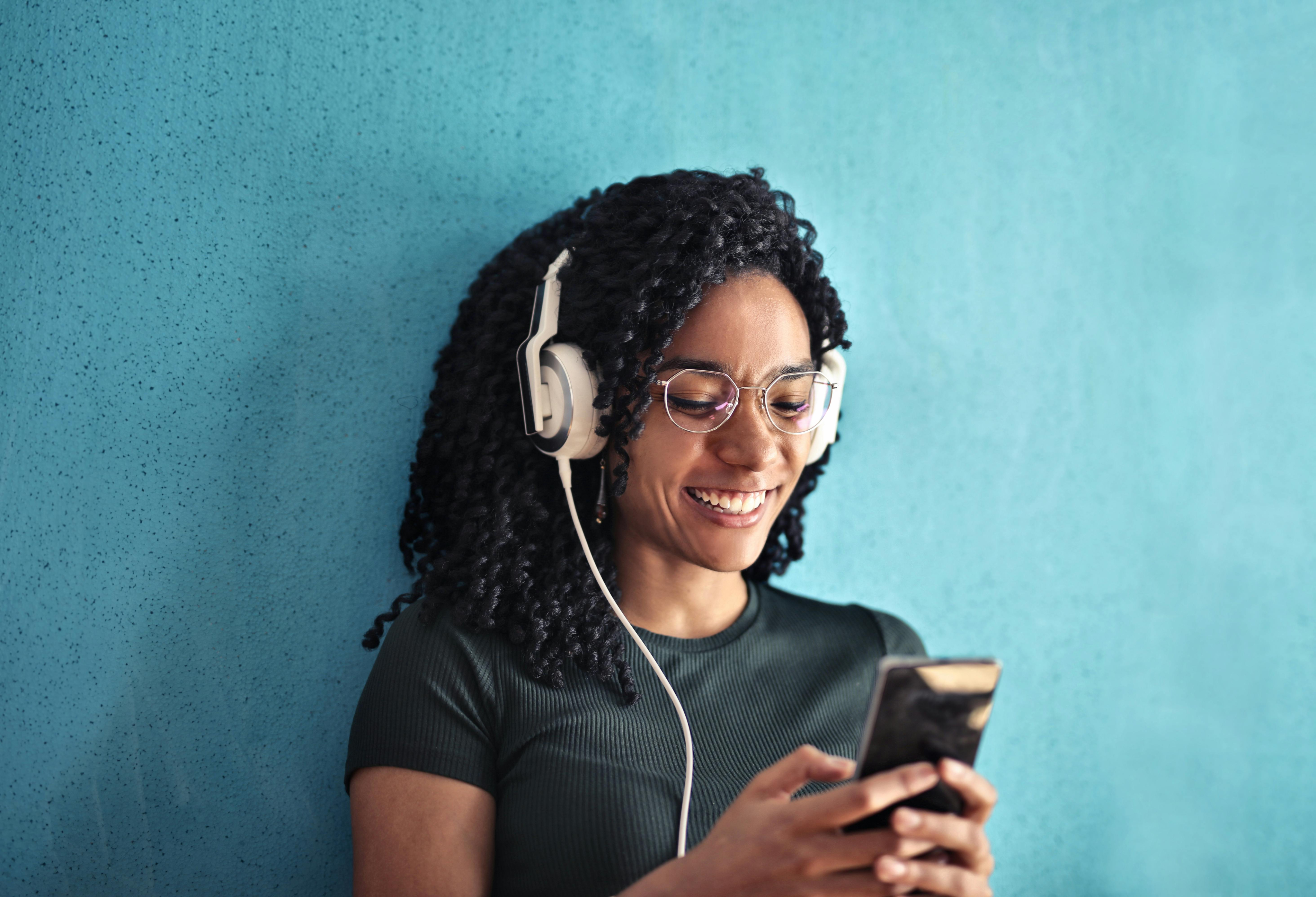 Woman holding phone listening to podcast through headphones