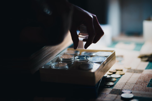Close up of a person's hand holding coins over a board. Photo by Yuri Krupenin on Unsplash.