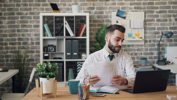 A man sitting at a desk with a laptop and papers. Photo by Vitaly Gariev.
