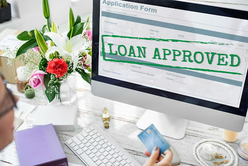 Loan approved concept with a hand holding a card and an iMac screen with the word "Approved" on it. Photo by rawpixel.com from Freepik