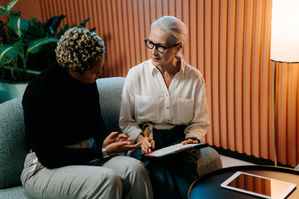 Two middle-aged women seated across each other talking